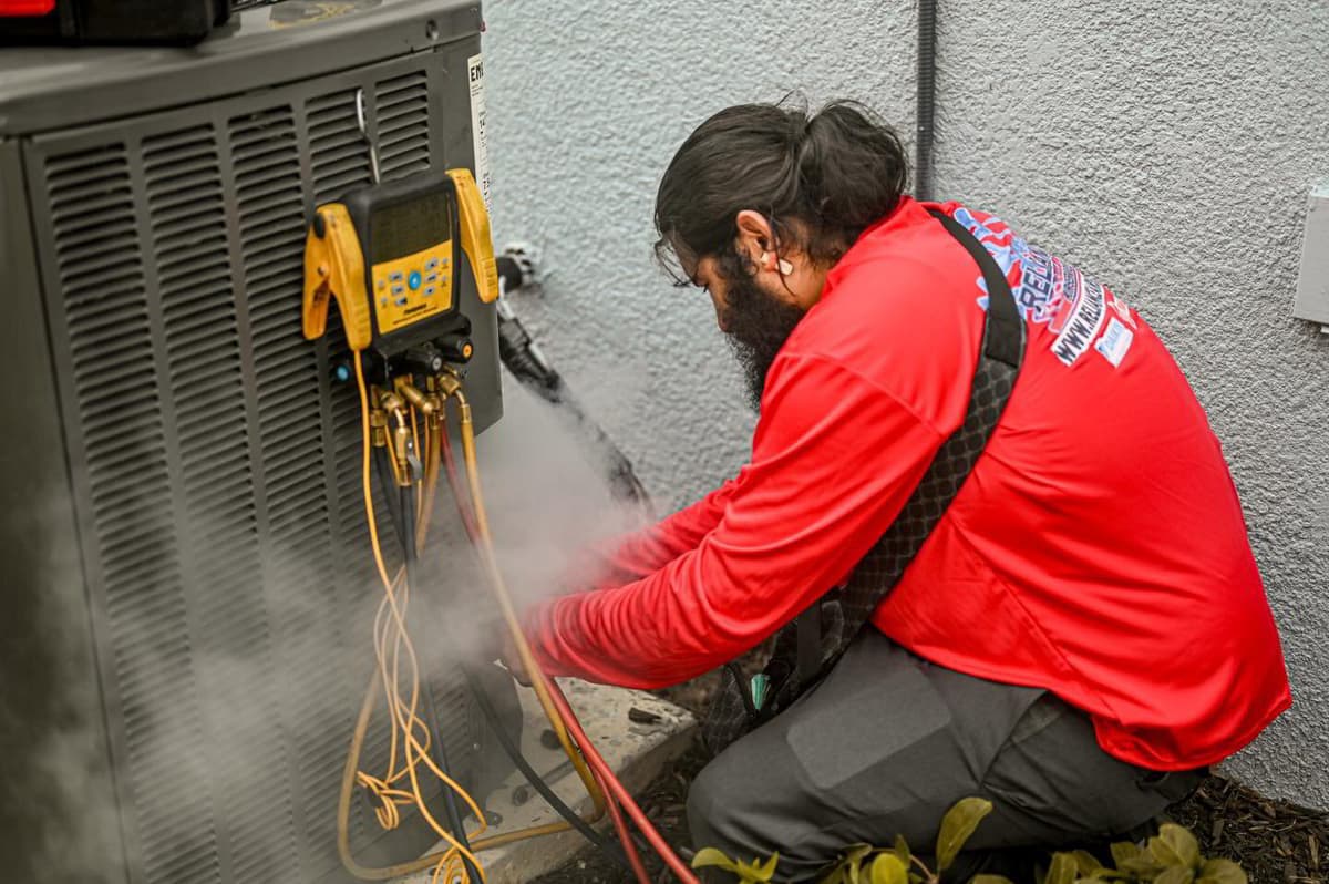 Technician checking refrigerant pressures on an outdoor AC unit